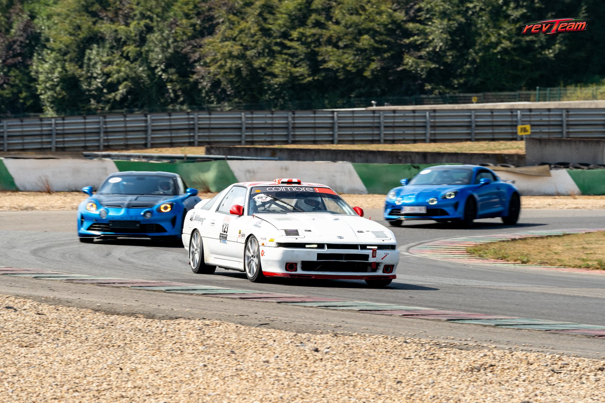 De Toyota Supra rijdt op circuit naast twee blauwe sportwagens